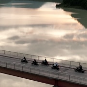 Several motorcyclists cross a bridge that is in the water